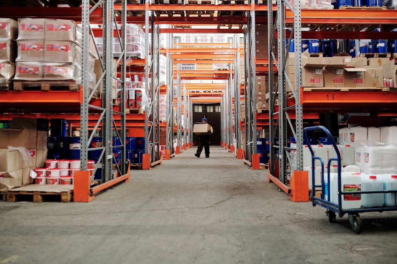 services-02 A worker carrying a box in a well-organized warehouse storage aisle.